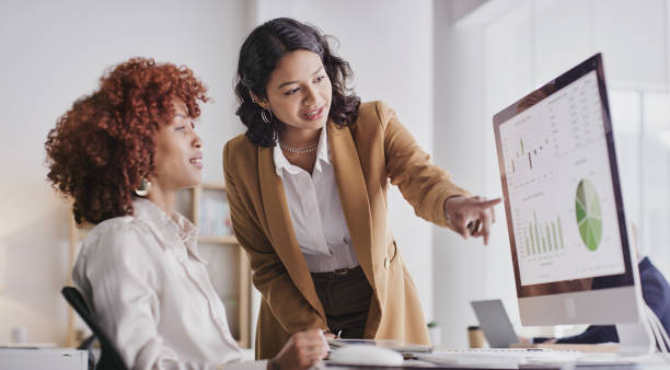 A woman pointing at something on the screen of a computer.